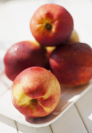 Peaches over white plate, over white wooden table, vertical imageの写真素材