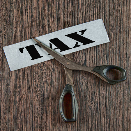 Scissors cutting the word tax written on a paper strip, over wooden background, square hdr imageの写真素材