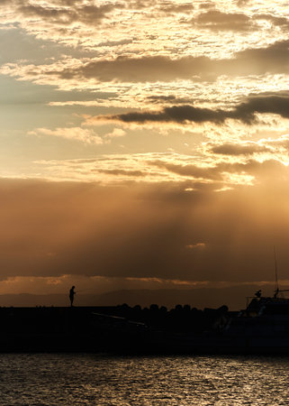 Silhouette of a fisherman at sunset in the port of Triesteの写真素材