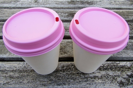 Two paper coffee cups with pink lids on wooden tableの写真素材