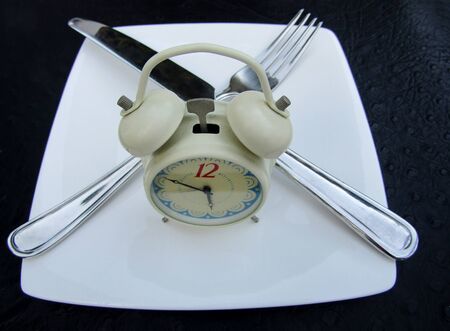 Twin bell alarm clock with white plate, fork and knife as fasting concept