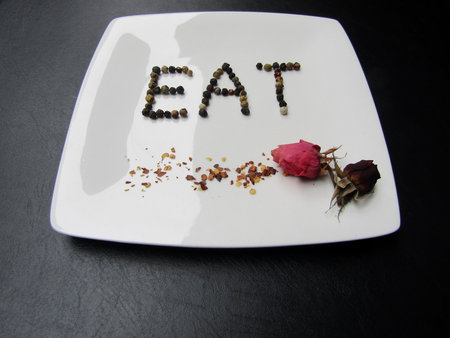 Plate with word `eat` made of black pepper, red chili pepper flakes and pink dried rose budsの写真素材