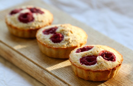 Three raspberry muffins on a wooden board close up