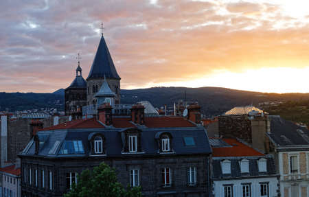 Bell tower of the church in Clermont Ferrand at sunset surrounded by buildings with red roofsの写真素材