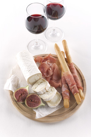 Red wine, goat cheese, parma ham, bread sticks on white backgroundの写真素材