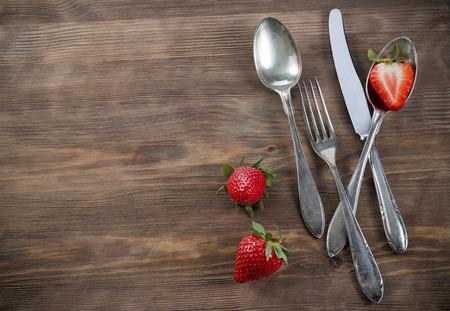Old spoons, fork and knife on wooden surface with strawberry for invitation and menuの写真素材