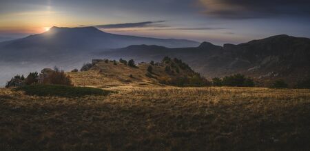 Sun hides behind the mountains. Sunrise or sunset. Flat area in the foregroundの写真素材