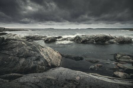 Waves of stormy sea break on rocky shore. Dramatic sky. Horizontal layout for travel storiesの写真素材
