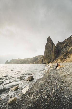 Female hiker with an orange backpack enjoying sea view. Rocky seashore. Coastline at golden hour....
