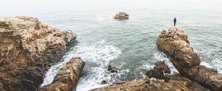 Man standing on a rock at the sea shore. Adventure photography. Panoramic image. Scenic viewの写真素材