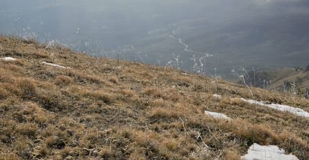 Close-up of dry grass. Winding road in the mountain valley. Horizontal layout for travel storiesの写真素材