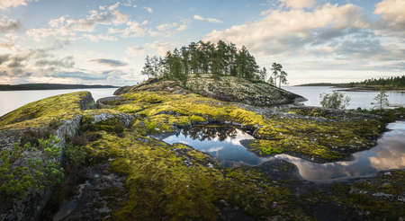 Small beautiful forested island in the middle of big lake. Scenic view of the coast during golden hour. Panoramic imageの写真素材