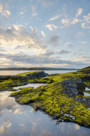 Sunrise over green rocky island. Clouds reflecting in water. Vertical layout.の写真素材