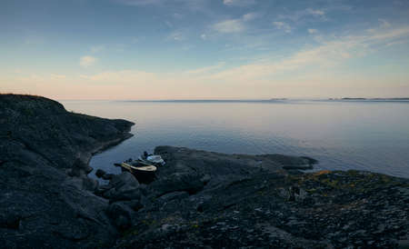 Old motor boats parked near rocky shore. Scenic view of water, rocks and sky at sunriseの写真素材