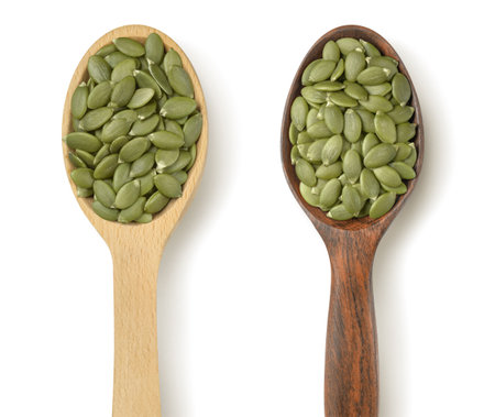Wooden spoons with green pumpkin seeds in the middle of pile isolated on white background. Package design element with clipping pathの写真素材