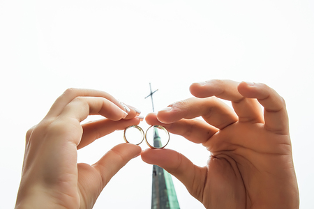golden wedding rings in the hands of the bride sheltered against each other against the backdrop of the church dome with a cross.の写真素材