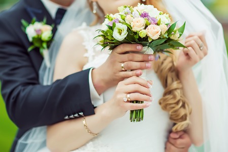Wedding bouquet with delicate pink, beige, white flowers with green leaves in the hands of the brides in dress and costume, couple in love.の写真素材