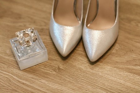shoes for the bride in silver and a bottle of perfume, formal high heel shoes, accessories on a wooden background, fashion and aroma concept, a pair of elegant women's shoes.の写真素材