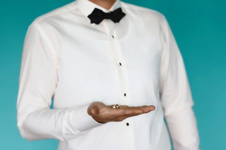 gold wedding rings in the hands of the bride in a white shirt and a black butterfly on a nude background.の写真素材