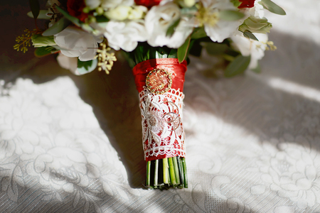gold wedding rings on a bouquet of flowers with white lace and a red ribbon and brooch.の写真素材