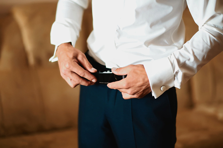 Grooms morning preparation, handsome groom getting dressed and preparing for the wedding, wearing a belt.の写真素材