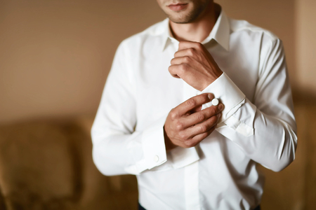 Grooms morning preparation, handsome groom getting dressed and preparing for the wedding, the bridegroom wears cufflinks in a white shirt.の写真素材