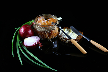 Pike caviar, roe in a glass jar, raw farm eggs, purple onion, green onions, bread with butter, fork and knife on a black background, close-up, set.の写真素材