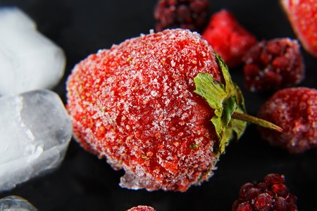 macro frozen strawberries, raspberry, blackberry, pieces of ice on a black shale board, frozen fruit, set.の写真素材