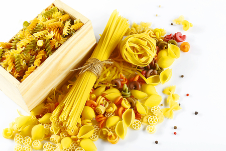 full wooden box of different raw Italian pasta spread pepper peas on white background, top view, place for text, set, flat lay.の写真素材