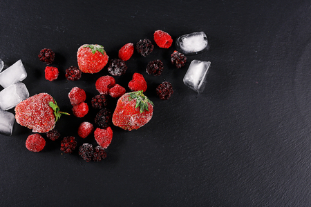 Frozen raspberry, blackberry, strawberries, pieces of ice on a black shale board, frozen fruit, top view, close up, place for text, set.の写真素材