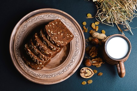 dark cereal bread with sunflower seeds, on a plate, scalded nuts, cup of milk, raisins on shale board, top view concept of healthy eating, set.の写真素材