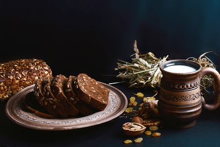 dark cereal bread with sunflower seeds, on a plate, scalded nuts, cup of milk, raisins on shale board, concept of healthy eating, place for text, set.の写真素材