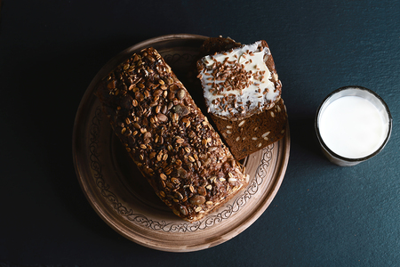 dark cereal bread with sunflower seeds, glass of milk, on a dark background shale board, concept of healthy eating, top view, set.の写真素材