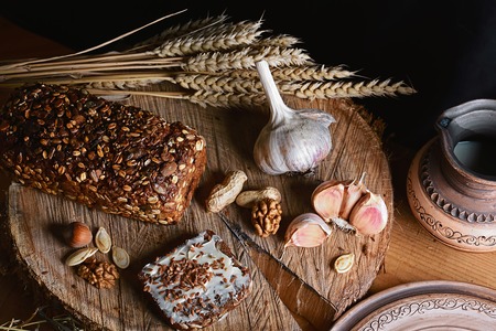 dark cereal bread with sunflower seeds, cup of milk, garlic and stems of wheat, nuts, concept of healthy eating, on a wooden background on a stump, top view, set.の写真素材