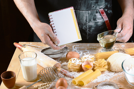 Chef with notepad text, ngredients for dough, cooking pasta tagliatelle spaghetti, including flour, eggs, milk, on wooden rustic background, set.の写真素材