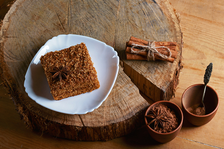piece of poured honey cake with cream on plate, decorated with anise, sticks of cinnamon and cocoa, on a wooden background on a stump, top view, set.の写真素材