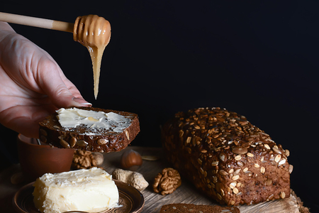 dark cereal bread with sunflower seeds smeared with honey and butter in hands, cup of milk, concept...