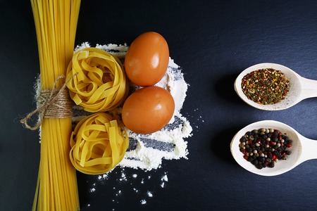 Different kinds of pasta tagliatelle, spaghetti, italian foods concept and menu design, raw eggs and flour on a shale board, empty space for text, top view, set.の写真素材