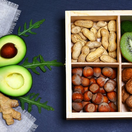 Green vegetables avocados, lemon, ginger, rucola salad, peanuts and hazelnuts in the box on a shale board, the concept of healthy eating, copy space, top view set.の写真素材