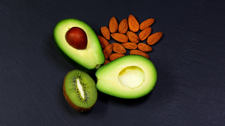 Green assortment vegetables and fruits, avocados, kiwi and almonds, nuts on a shale board, the...