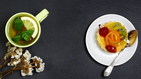 cake, sweet fruit dessert with orange and kiwi, jelly, cup of tea, flowers on a napkin on a shale board, the concept of healthy eating, copy space, top view set.の写真素材