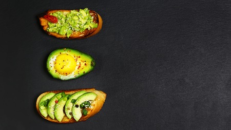 Healthy lunch snack, three delicious avocado sandwiches, fresh sliced avocados copy space on a black...