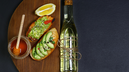 Healthy lunch snack, avocado sandwiches made with fresh sliced avocados, honey, oil, lemon on a wooden board copy space on a black stone background, copy space, top view, set.の写真素材