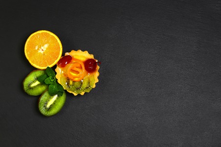 Variety of fruits oranges, kiwi, lemon, mint, cake, sweet fruit dessert bunched together on a shale board, the concept of healthy eating, copy space, top view set.の写真素材