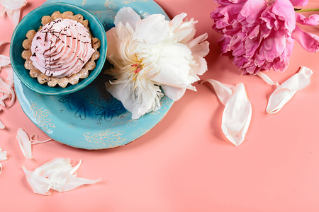 Picturesque still life in pink tones, decorative plate with creamy cake surrounded by white petals pions, nearby is a pink flower, on a pink background, copy space, top view, set.の写真素材