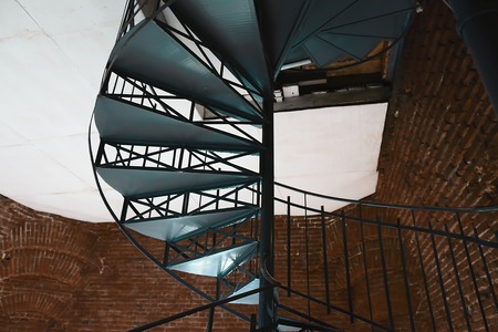 Forged iron twisted stairs with reflection on a red brick wall.の写真素材