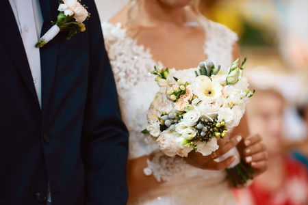 Wedding bouquet with delicate pink, beige, white flowers with green leaves in the hands of the brides in dress and costume, couple in love.の写真素材