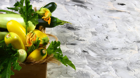 set of fresh colored zucchini in a wooden box, blossoms and green leaves on a white table. zucchini background. Flat lay. Copy space.の写真素材