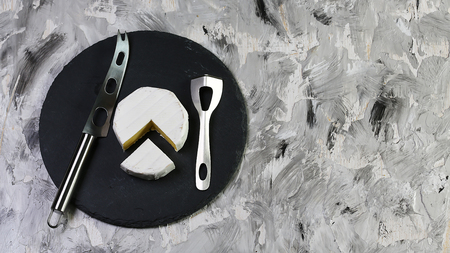 Piece of cheese camembert or brie in paper on a round shale board tasting with knives for cheese. copy text. Flat top view, from above.の写真素材