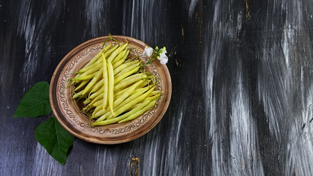 long yellow bean on a clay plate with leaves and a bloom on a dark background. Food recipe on wooden background. Flat top view.の写真素材